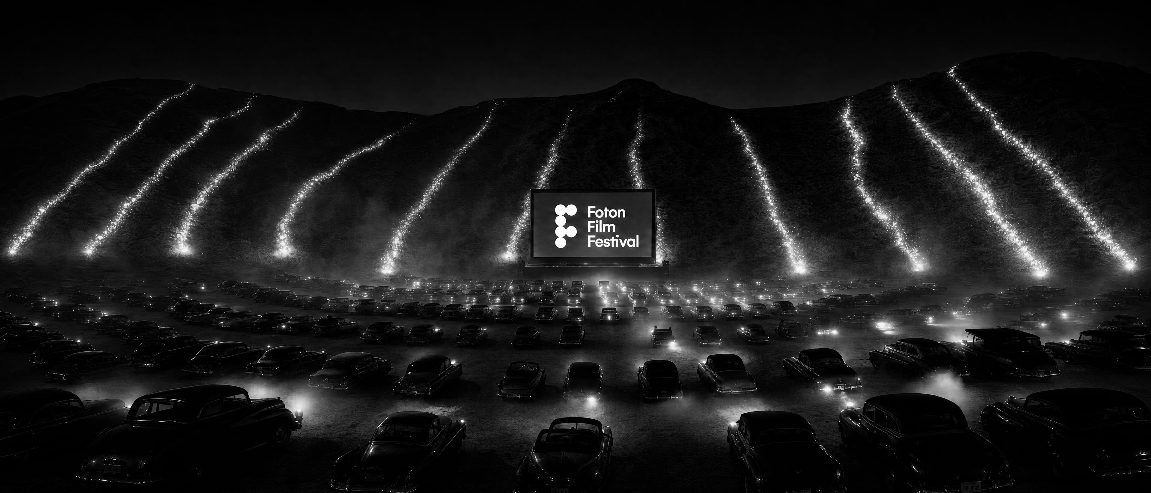 Skena e FOTON FILM FESTIVAL natën: lumenj drite zbresin kodrës drejt ekranit, mbi një det veturash të parkuara.